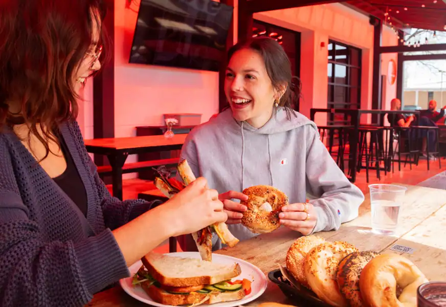 Two women sitting on the fuoco patio eating bagels and sandwiches