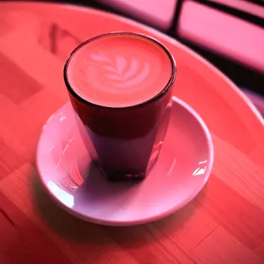 Glass of latte with leaf latte art on a white saucer