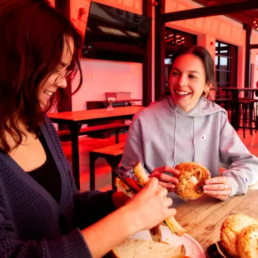 Two women sitting on the patio of Fuoco holding sandwiches and bagels
